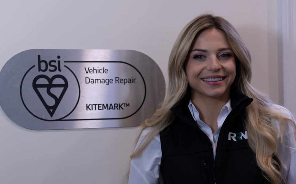 Accreditations Alex Gray standing next to bsi Vehicle Damage Repair Logo on wall